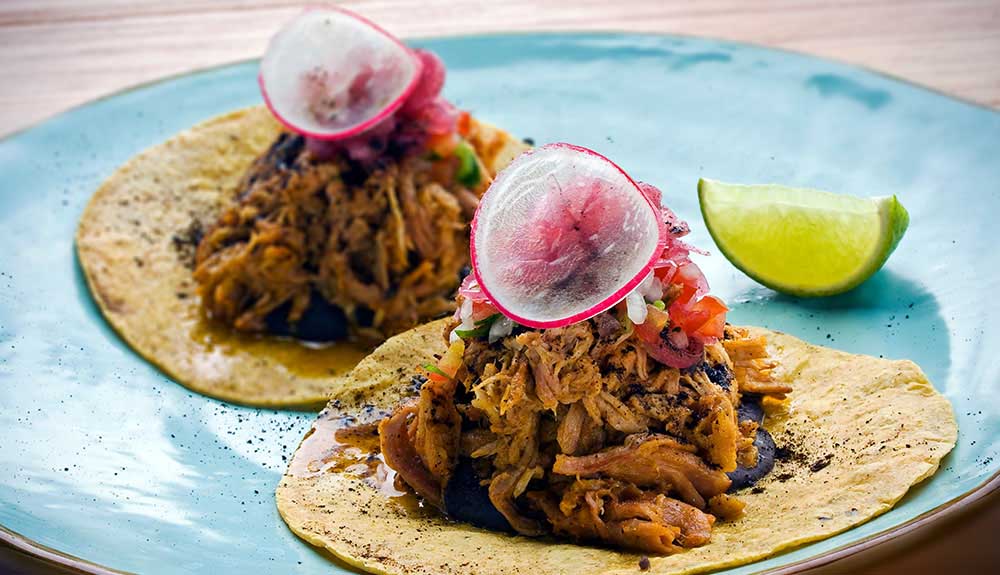 Two delicious looking authentic Mexican tacos garnished with radish and lime on the side