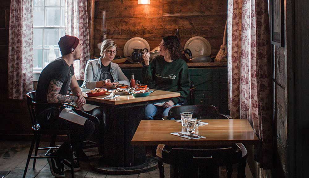 A man with a beanie and two women sit inside an adorable historical spot enjoying delicious food