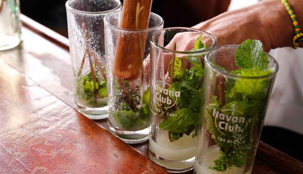 A bartender muddles mint in cocktail glasses