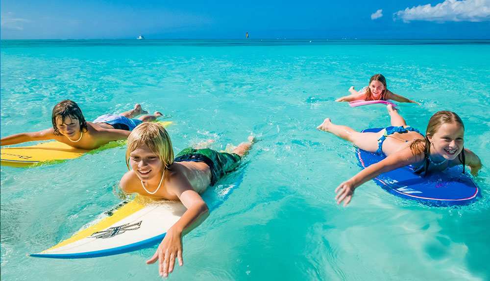 Four kids lying on their bellies on surfboards in the Caribbean water