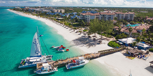 Three boats anchored along a pier that stretches over the Caribbean ocean and white sand