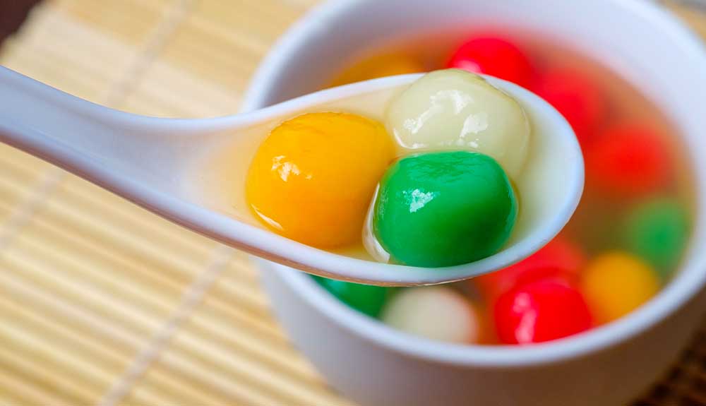 A spoon holds three tangyuan, yellow, green and white rice balls