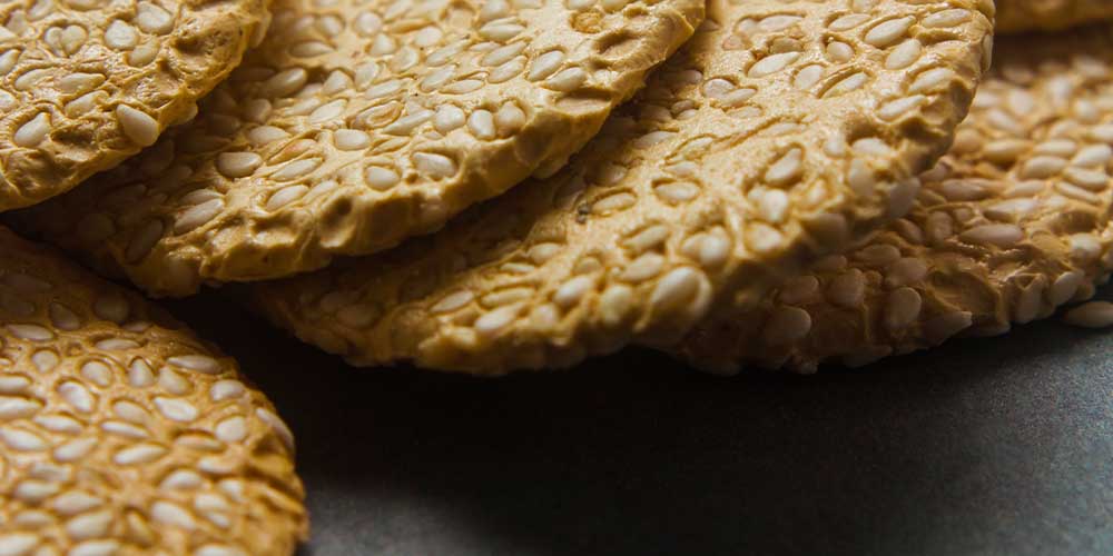 A close up photo shows five thin sesame crackers on a table