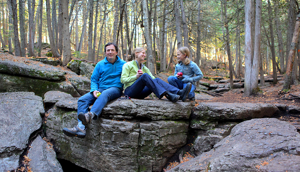 A family takes a break from their hike to eat an apple in the Kawarthas Northumerland region of Ontario.