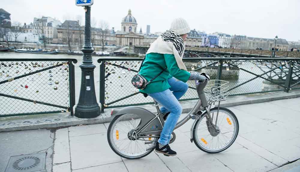 A woman cycles on a bridge in Paris, France