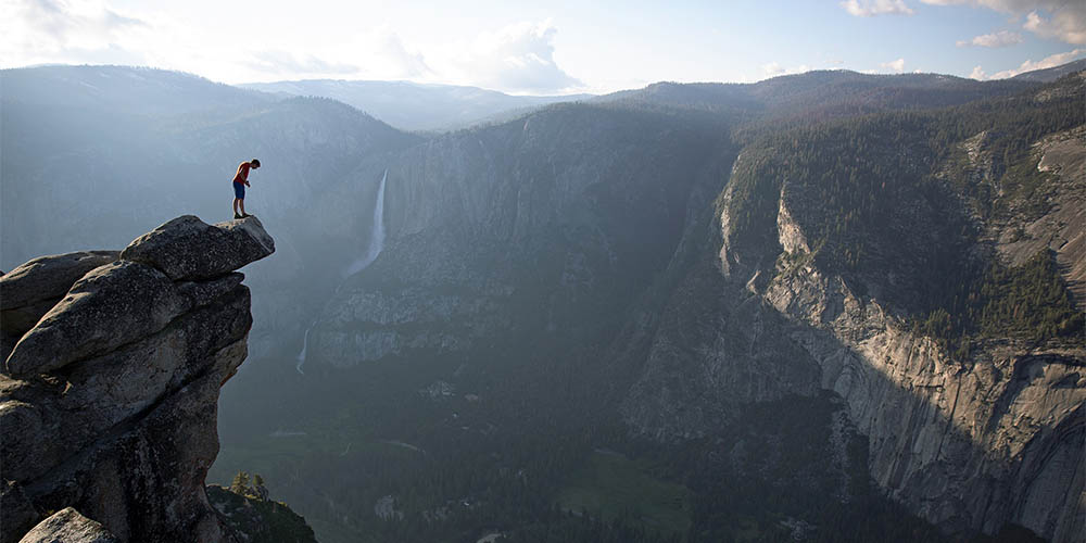 A hiker stands on the edge of a precipice over a mountain range