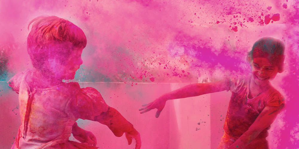 Two children are shown throwing bright purple powder at each other during Holi
