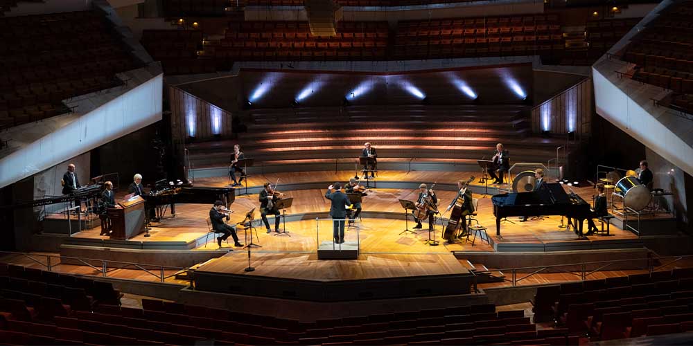 Musicians in a small orchestra are shown spread out on a stage