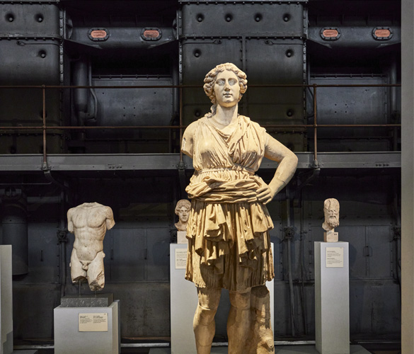 A statue of a woman inside a museum. In the background, there are other statues and busts.