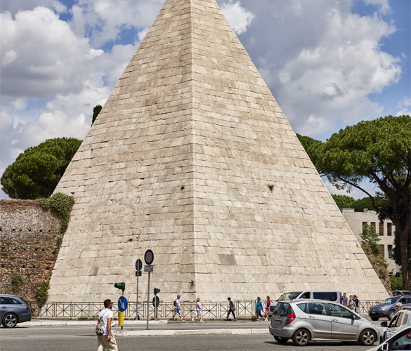A cream-coloured pyramid in front of a cloudy, blue sky.
