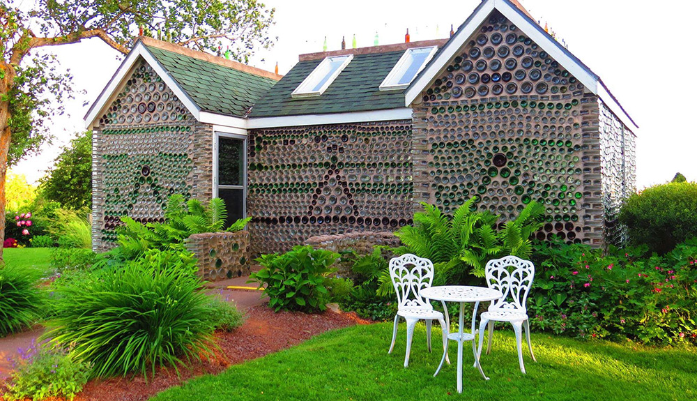 The bottle houses in Cape Egmont and Point Prim are seen, the grounds they're built on lush and green and a small white patio set sits in front