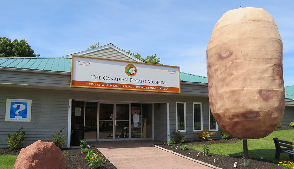 The Prince Edward Island Potato Museum entrance is seen on a bright day, a large statue of a potato stands tall beside the front doors