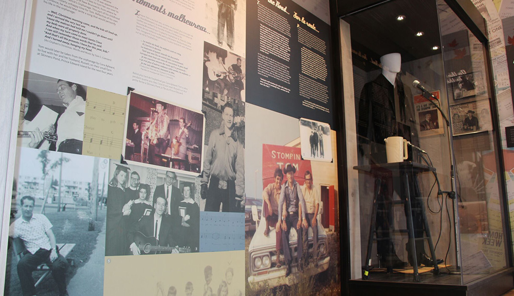 The museum wall of the Stompin, Tom Conners Centre and a mannequin dressed in all black, a microphone placed in front of it 