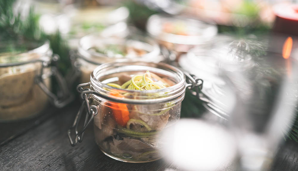 A table is laid out with several small glass jars. Each one is filled with some pickled herring and onions.