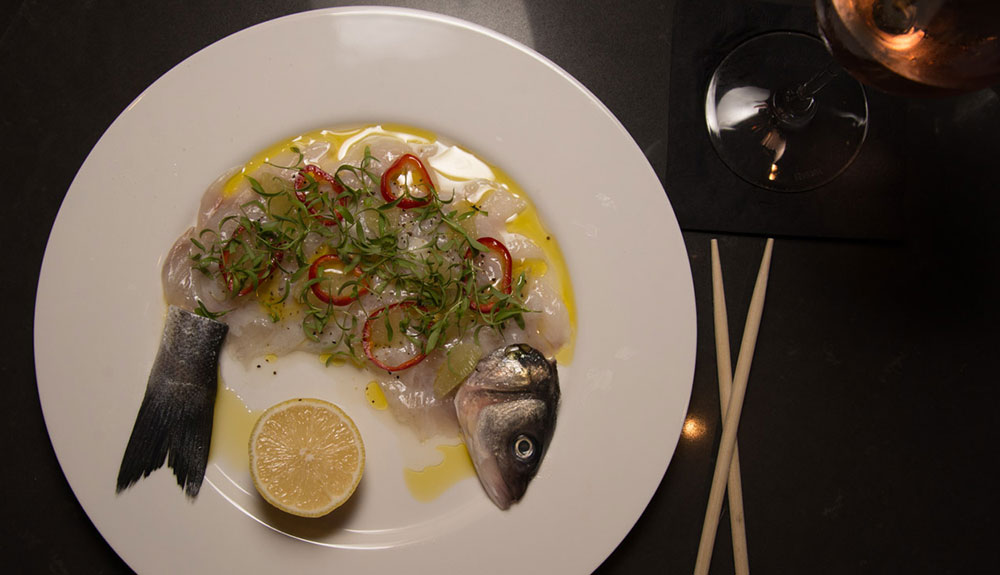 Whole-fish ceviche served on a plate, garnished with a lemon wheel with chopsticks on the side