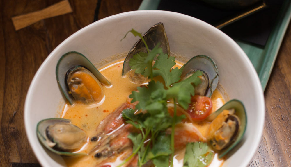 Bowl of coocnut curry seafood stew made with prawns and lined with mussels