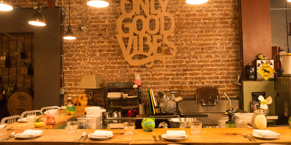 'Only good vibes' on an exposed brick wall in a restaurant in Oahu, with tables set to serve
