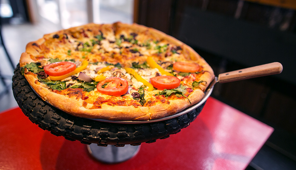 A personal pizza topped with veggies sits atop a custom-made tire-spoke platter at Riders Pizza