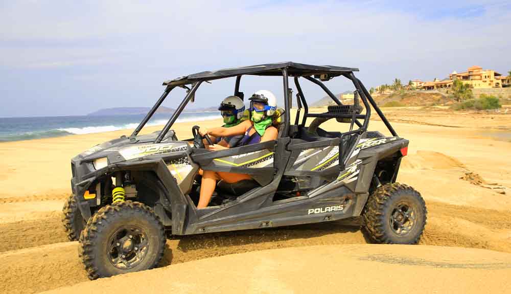Two people driving four-wheelers across the sand