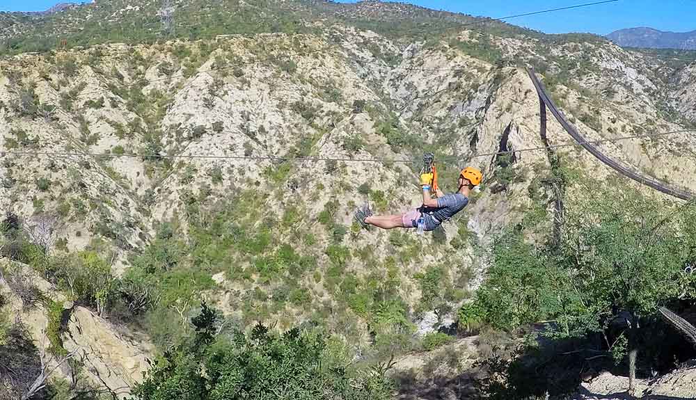 Man wearing a helmet zip lining across a canyon