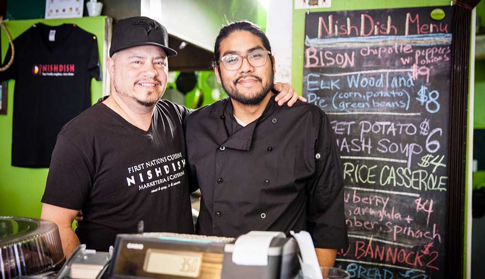 Two Indigenous men smile from behind the till at Nish Dish Marketeria in Toronto