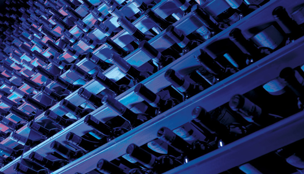 Dozens of wine bottles are seen stacked in a dim cellar