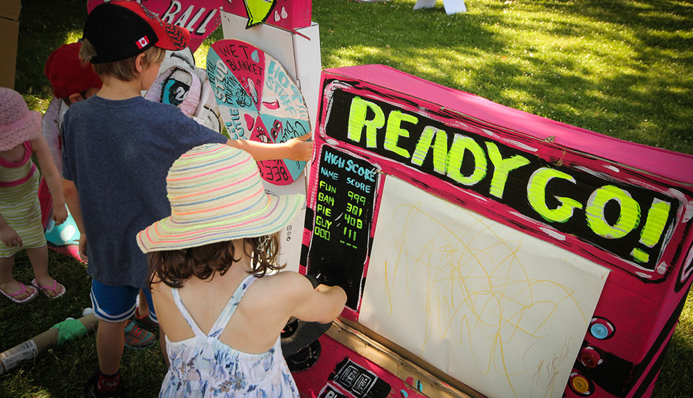 Two young children play on hand constructed arcade games made of brightly coloured cardboard