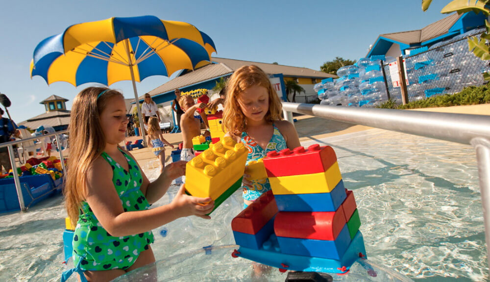 Little blonde girl and little red hair girl play with big Lego blocks in the water