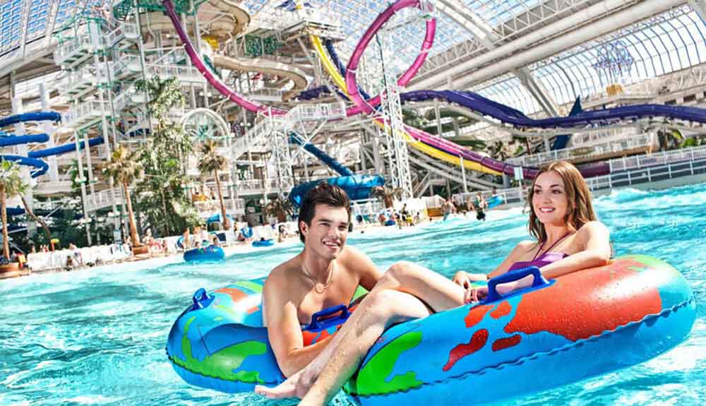 A man and woman float close together on water tubes with waterslides behind them