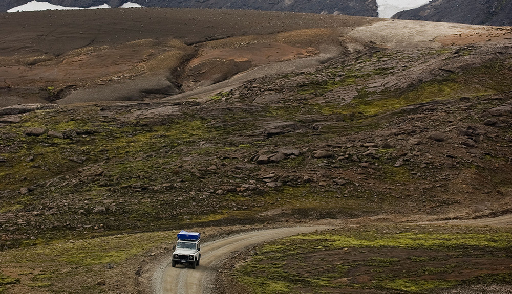 A jeep drives down a dusty winding road 