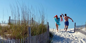 A man and woman swing a small child in their arms as they walk down a sand path to a Florida beach front