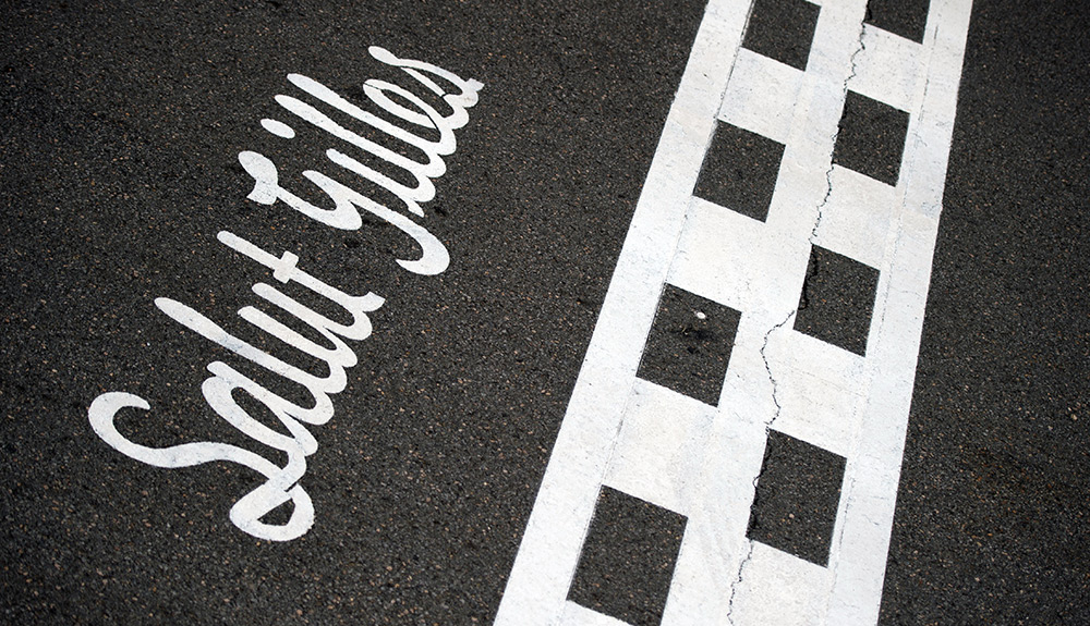 A black and white photograph of the smooth pavement at the Canadian Grand Prix, the paint reading Salut Gilles