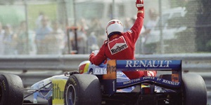 A race car driver in a red race suit and white helmet raises his fist in victory at the Canadian Grand Prix