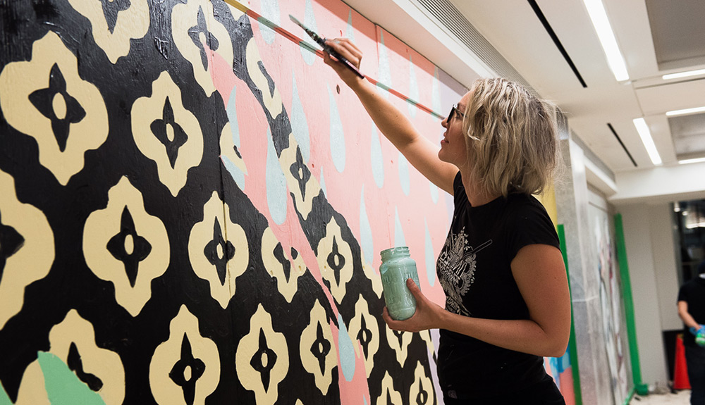 Blonde woman with short hair and glasses paints the wall