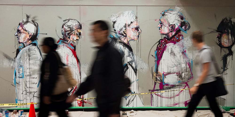 Three people walk quickly by an impressive mural of people walking from the side