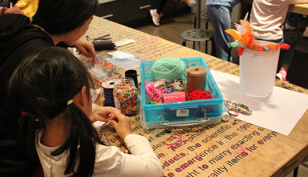 Woman and little girl play with crafts like yarn and beads on a wooden table