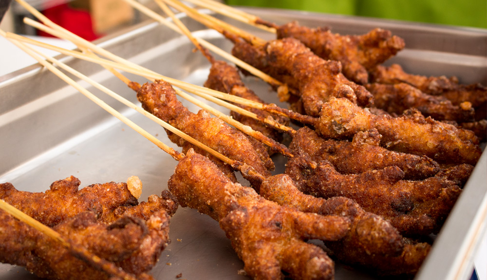 Golden brown deep fried chicken feet threaded onto wooden skewers are stacked in a metal tray as seen at the CNE