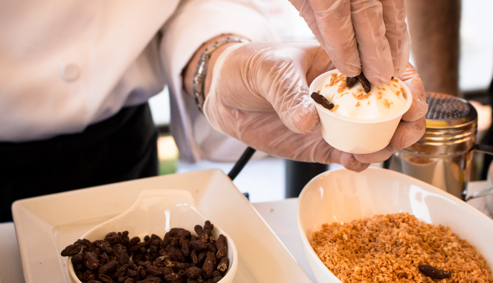 A person tops a vanilla soft serve ice cream with fried crickets and golden toasted coconut, as seen at the CNE