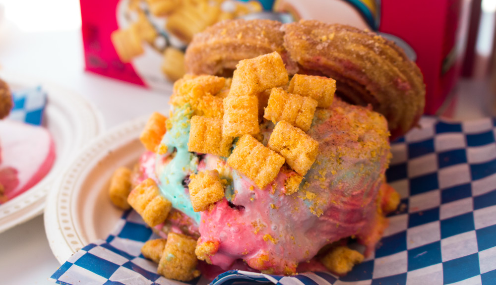 An ice cream sandwich made with two sugared churros sandwiching a generous scoop of multicoloured ice cream, all sprinkled with Captain Crunch cereal, as seen at the CNE