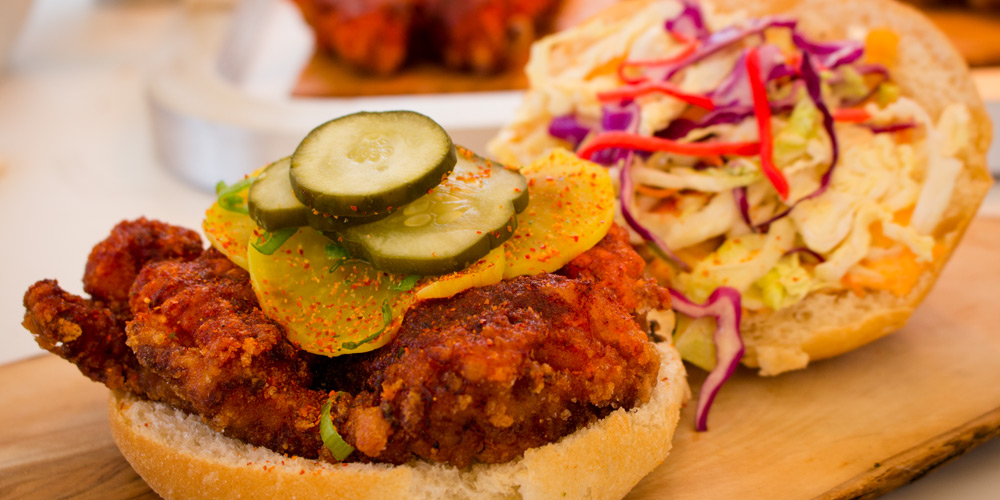 Closeup shot of CNE fare, a fried chicken sandwich topped with pickles, the top bun laid out beside it, topped with a colourful and crunchy slaw