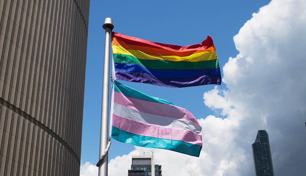 The rainbow Pride flag and Trans flag are seen flying high on a bright summer day