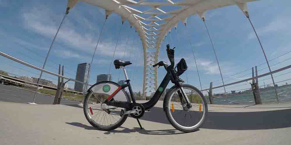 A bike in the centre of the frame with the green Bike Share Toronto logo on its rear wheel. Lake Ontario and some office towers can be seen in the background.