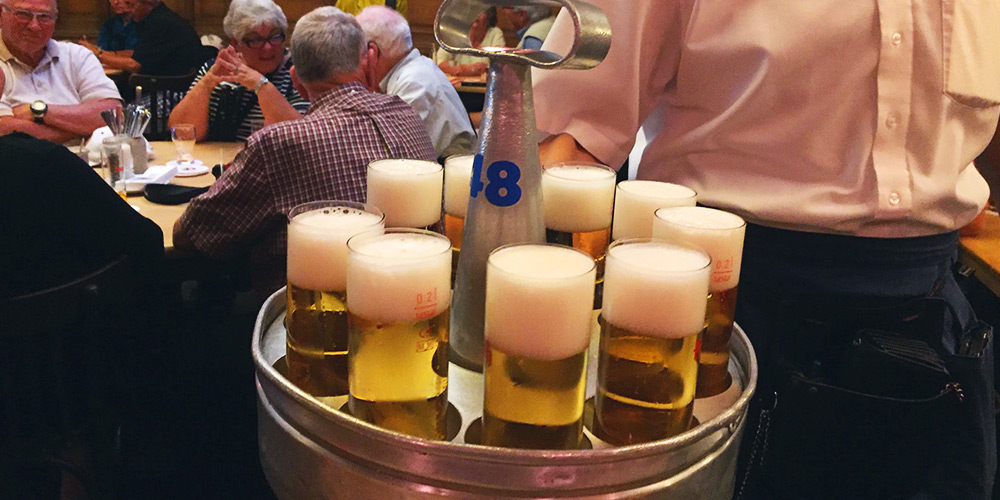 A neat tray with a handle carrying 9 glasses of Kolsch beer