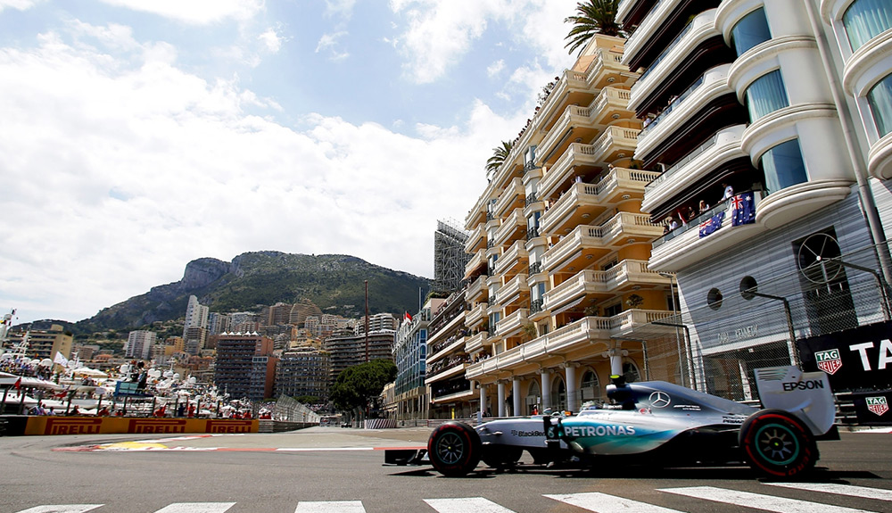 A blue Formula 1 car races down a track in the streets of Monte Carlo, Monaco as spectators watch from their balconies
