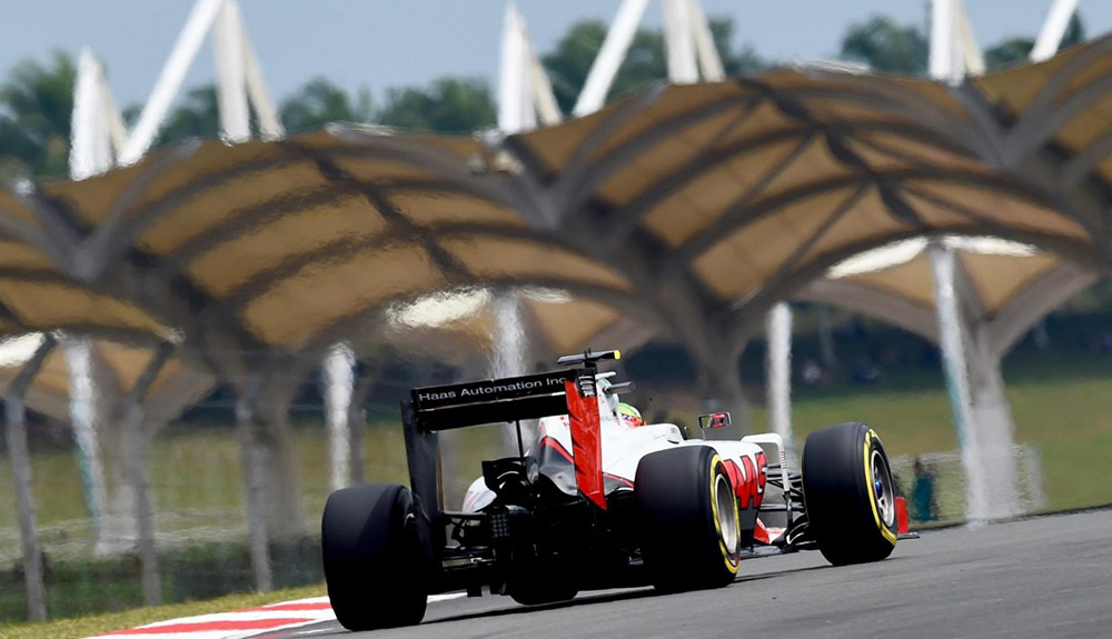 A red, white and black Formula 1 car drives down a track, the background blurred because of the speed in Sepang, Malaysia