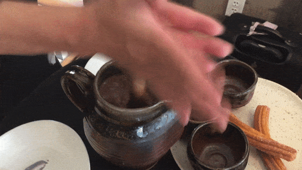 Hands are shown rubbing a stick to quickly stir sauce in a pot with a handle