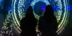 The silhouette of two people is visible. They are looking at a spiral circle of lights that fade from blue to white to yellow to a light pink.