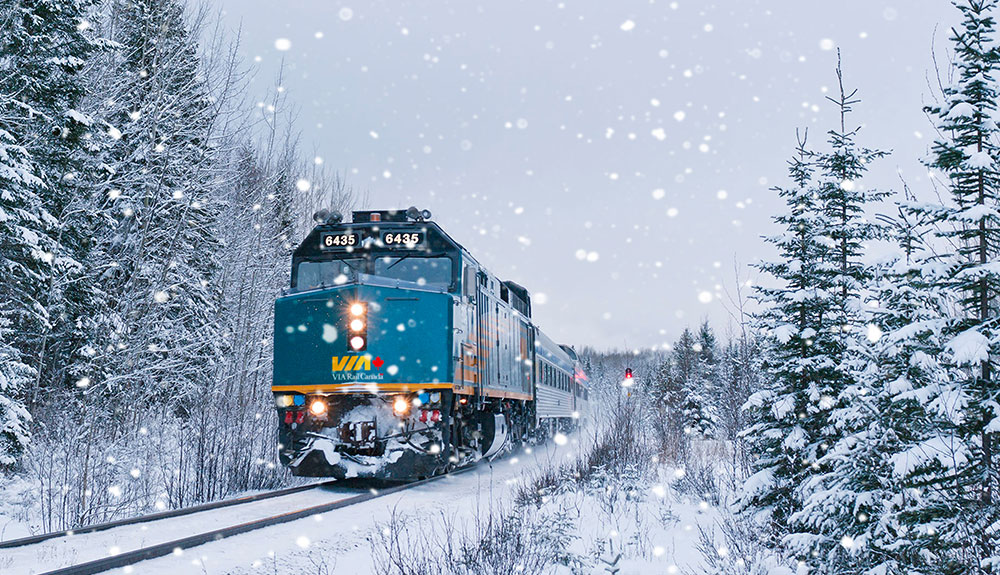 Front of a VIARail train in the snow chugging along the tracks