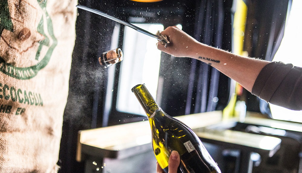 The top of a champagne bottle is sliced off with a knife