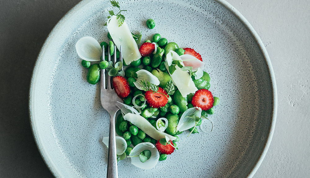 A fork rests on a plate with greens, cheese and strawberries in the center